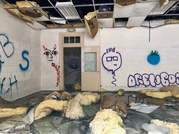 Ein Raum mit Graffiti an den Wänden, eine Tür im Hintergrund, Deckenstangen und Lampen sowie verstreute Gegenstände auf dem Boden, die tragische Ereignisse im Detroit-Bereich symbolisieren.