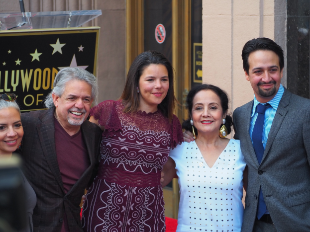 Gruppe von Menschen auf einem roten Teppich bei der Zeremonie der Hollywood Walk of Fame mit einer Kamera auf der linken Seite, einer Tafel mit Text, einem Glaspodest und einer Wand im Hintergrund.