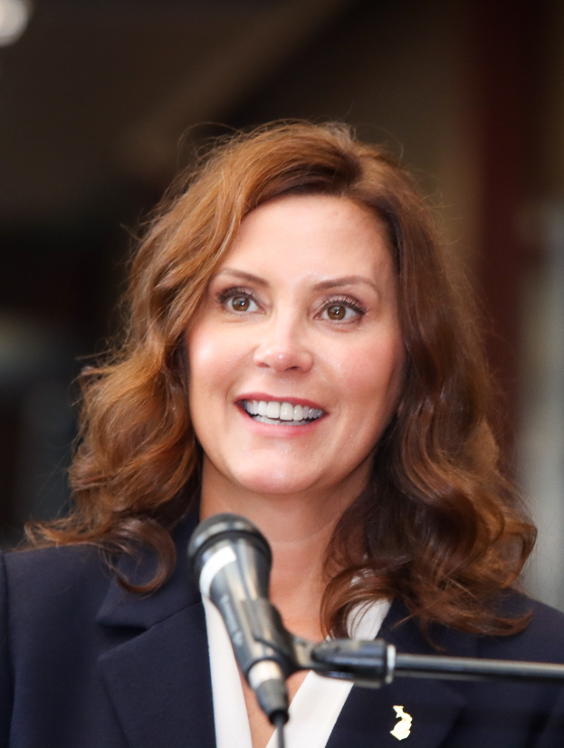 Michele Bachmann, gekleidet in Anzug und Krawatte, spricht in ein Mikrofon mit unscharfem Hintergrund.