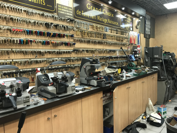 Ein unordentlicher Garage-Workshop mit verschiedenen Werkzeugen, Maschinen, Schränken und Texttafeln an den Wänden und auf dem Boden, darunter eine Uhr und Deckenleuchten.