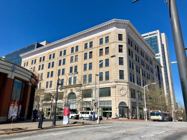 Großes Gebäude mit vielen Fenstern als Washington Post Office identifiziert, umgeben von Straßenmasten, Straßenlaternen, Kraftfahrzeugen, Fußgängern, Informationsschildern, Bäumen und einem bewölkten Himmel.