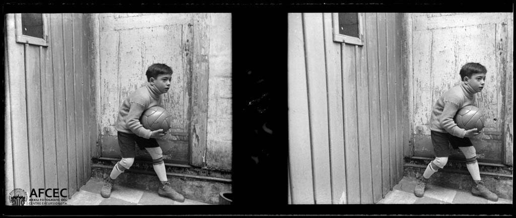 Ein junger Junge in Schwarz-Weiß hält einen Fußball vor einer hölzernen Tür.