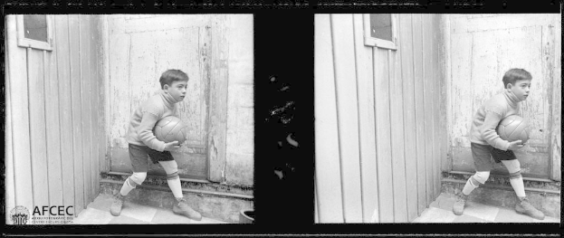 Ein junger Junge in Schwarz-Weiß hält einen Fußball vor einer hölzernen Tür.