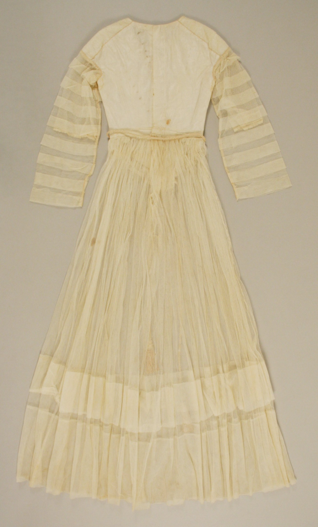 Ein weißes, langärmeliges Kleid mit einer gerüschten, voluminösen Schleppe auf einer weißen Oberfläche, das einen leichten Schimmer und eine hohe Taille aufweist.