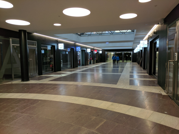 Langer Flur mit Menschen, die gehen, Deckenleuchten, Säulen, Glastüren und Informationsschildern, die an ein Rathaus erinnern.