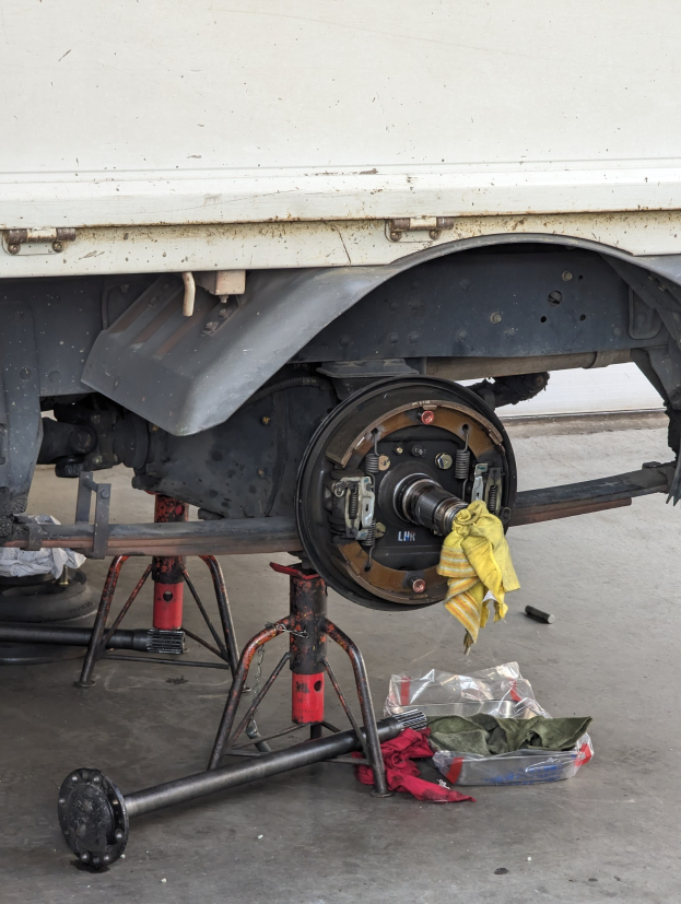 Ein gelbes Tuch über einem Lastwagen drapiert, der in einer Garage geparkt ist, mit Werkzeugen und Gegenständen, die vor ihm auf dem Boden verstreut sind.