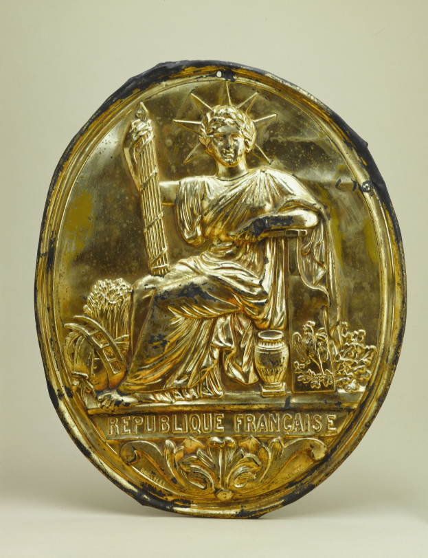 Goldene runde Plakette mit einer Miniatur-Statue der Freiheitsstatue und eingraviertem Text auf einem weißen Hintergrund.