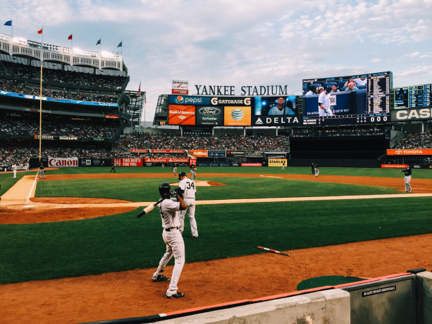 Baseballspiel im Gange im Yankee Stadium mit Spielern auf dem Feld und Zuschauern in den Rängen bei bewölktem Himmel.