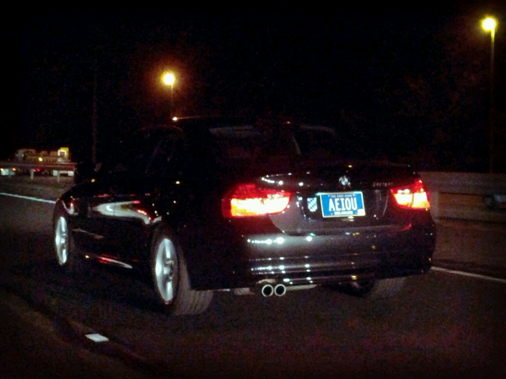Ein schwarzes Auto mit Lichtern und einer Aufschrift befindet sich in der Mitte einer Straße, mit einem schwarzen Hintergrund mit Lichtern.
