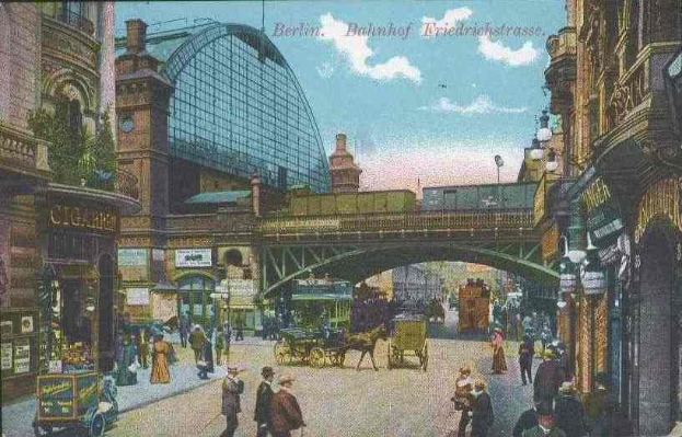 Alte Postkarte einer belebten Straßenkreuzung in Berlin, Deutschland, mit Fußgängern, Pferdefuhrwerken, Gebäuden, Laternenpfählen, einer Brücke und einem bewölkten Himmel, mit Text oben.