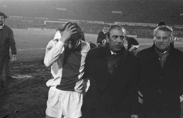Eine Gruppe von betrübten Männern in Schwarz-Weiß-Kleidung steht zusammen auf einem Fußballfeld, mit einem Stadion im Hintergrund, wahrscheinlich nach einem gewonnenen Spiel.
