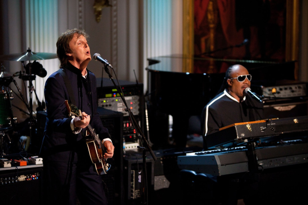 Paul McCartney und Stevie Wonder performen auf der Bühne bei den Grammys, wobei McCartney Gitarre spielt und singt und Wonder eine Brille trägt, während er am Piano spielt.