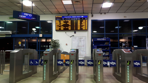 Flugzeugterminal mit einem Mann vor einer Metalldetektorschleuse, Metalldetektoren, Informationsschildern, einem Topf mit einer Pflanze, einer Wandtafel, einer Decke mit Leuchten und einem Anzeigebildschirm.