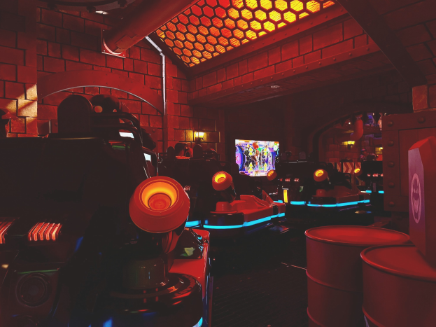 Ein hell erleuchteter Raum voller verschiedener Arcade-Videospielautomaten, Bildschirme und andere Geräte, die eine lebendige Atmosphäre schaffen.