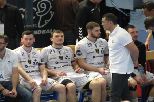 Eine Gruppe von Männern sitzt auf einer Bank, einige halten Flaschen, mit einem Banner im Hintergrund, auf dem "Nordkraque vs Bordeaux" steht.