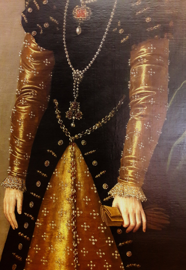 Bild einer Frau in einem goldenen Kleid mit hohem Halsausschnitt und langen Ärmeln, die eine Tasche hält.