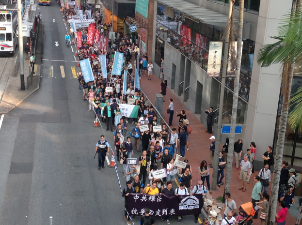 Eine große Gruppe von Menschen marschiert auf einer Straße in Hong Kong, hält Schilder und Plakate.