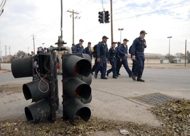 Gruppe von Polizisten in Uniform, die eine Straße mit Strommasten und Gebäuden entlanggehen, unter einem klaren blauen Himmel.