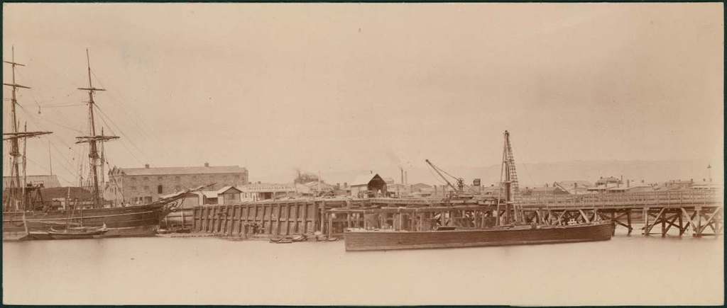 Eine Szene mit Wasser, Booten, Geb├Ąuden, Strommasten und einem Himmel im Hintergrund.
