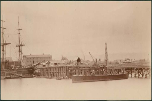 Eine Szene mit Wasser, Booten, Geb├Ąuden, Strommasten und einem Himmel im Hintergrund.