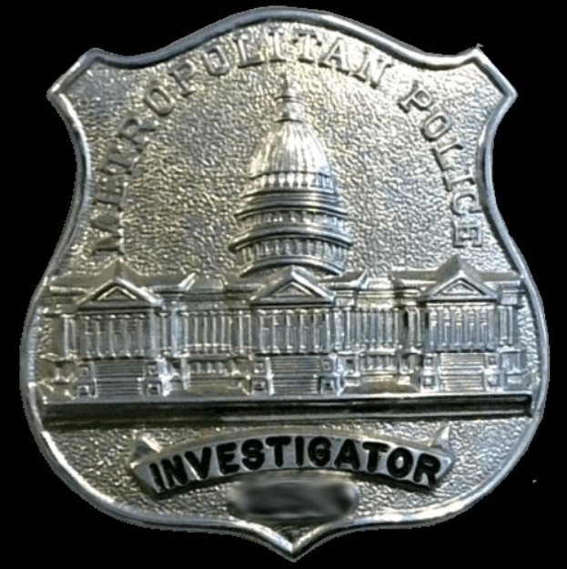 Ein silbernes Polizeischild mit dem Wort "Ermittler" darauf vor einem weißen Hintergrund.
