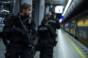 Polizeibeamte in schwarzen Uniformen, einige mit Waffen, stehen auf einem Bahnsteig mit beleuchteten Lichtern und Säulen im Hintergrund.