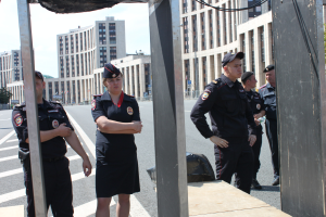 Eine Gruppe von Polizisten in Uniform auf einer Straße mit Polen und Drähten im Vordergrund, Gebäuden, Bäumen und einem klaren blauen Himmel im Hintergrund.