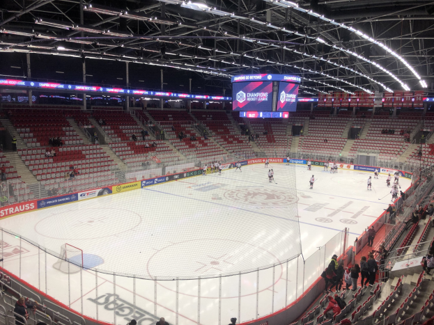 Ein Eishockeyspiel in einer großen Arena mit Zuschauern, einem Zaun um die Eisfläche, einem Bildschirm mit der Aufschrift "St. Louis Blues vs Detroit Red Wings", Metallrahmen und einer Decke mit Leuchten.