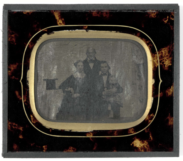 Schwarze-weiße Fotografie eines Mannes in Anzug und Krawatte und einer Frau in unbekannter Kleidung, die vor einem Fernseher stehen und ernste Gesichter haben.